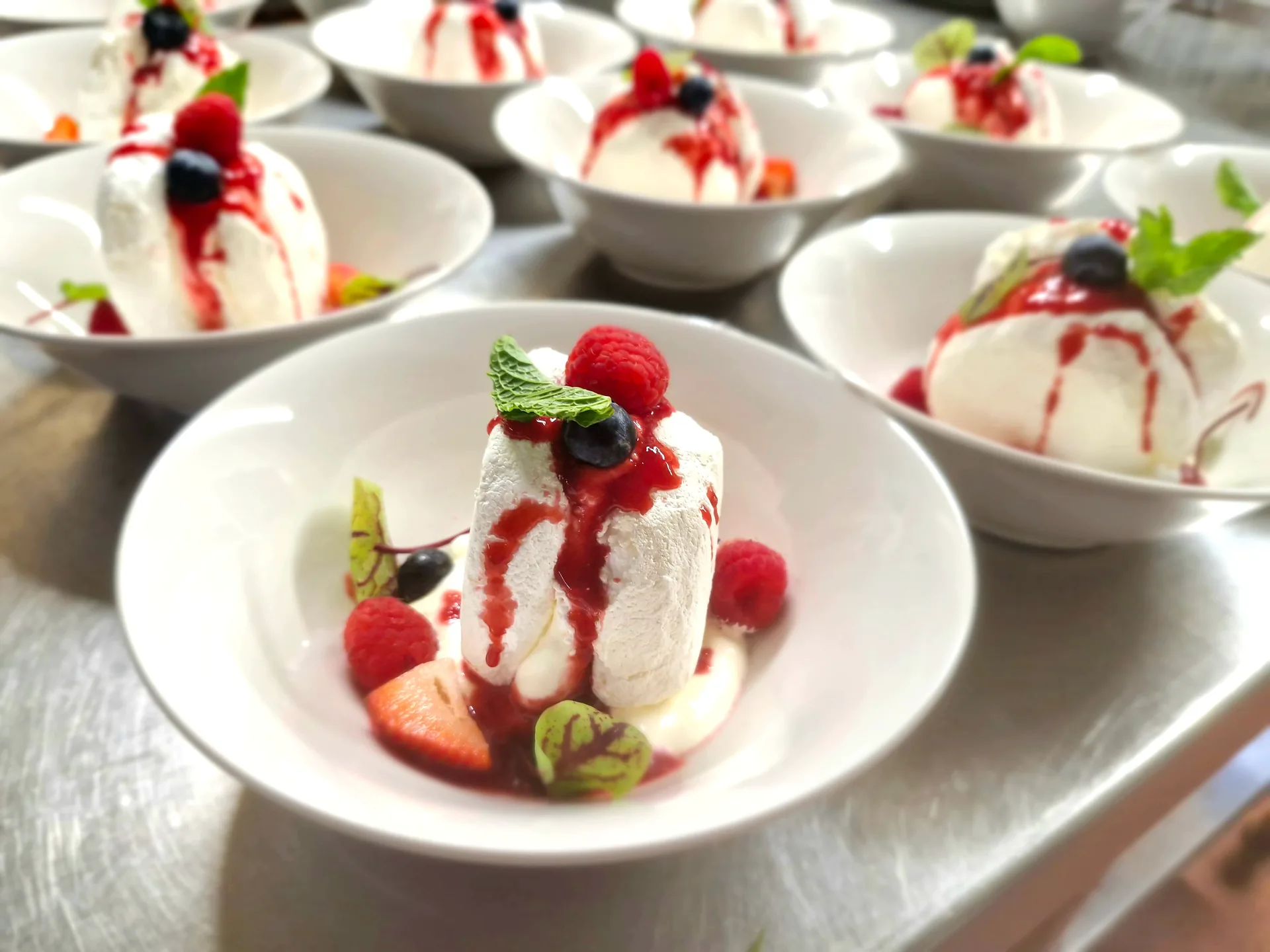 Rows of individual pavlovas with cream and berry coulis plated for a function