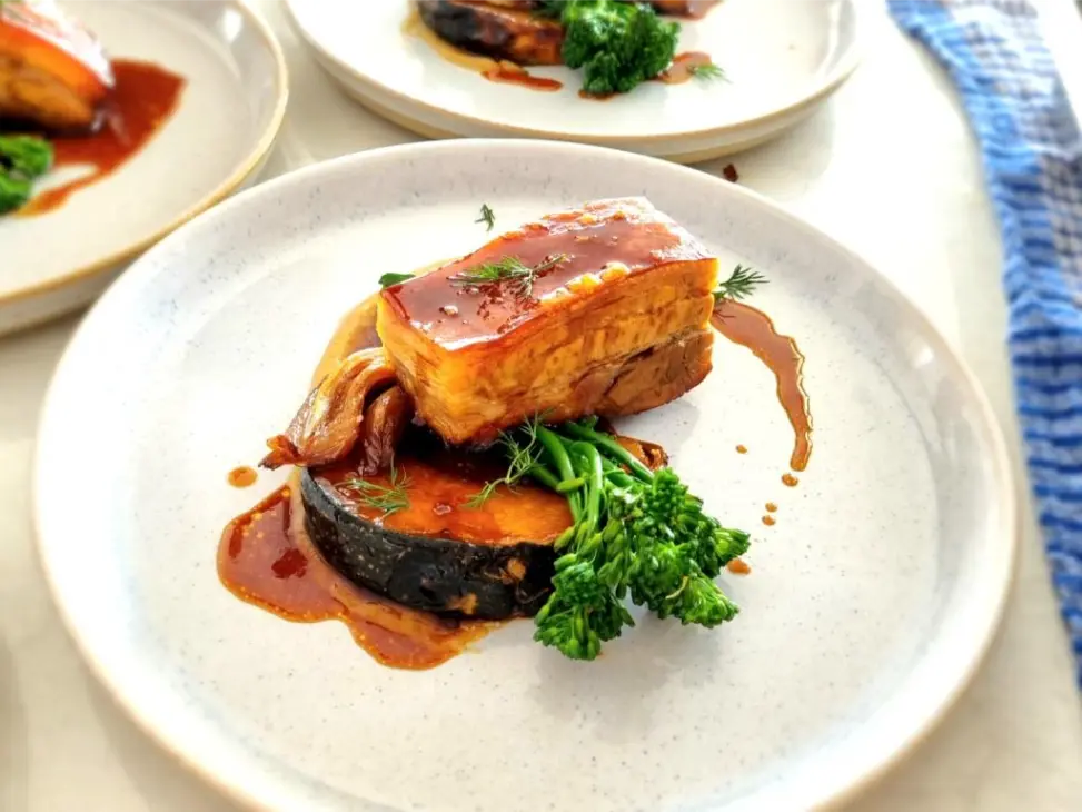 Glazed pork belly bites with herbs on a white serving plate