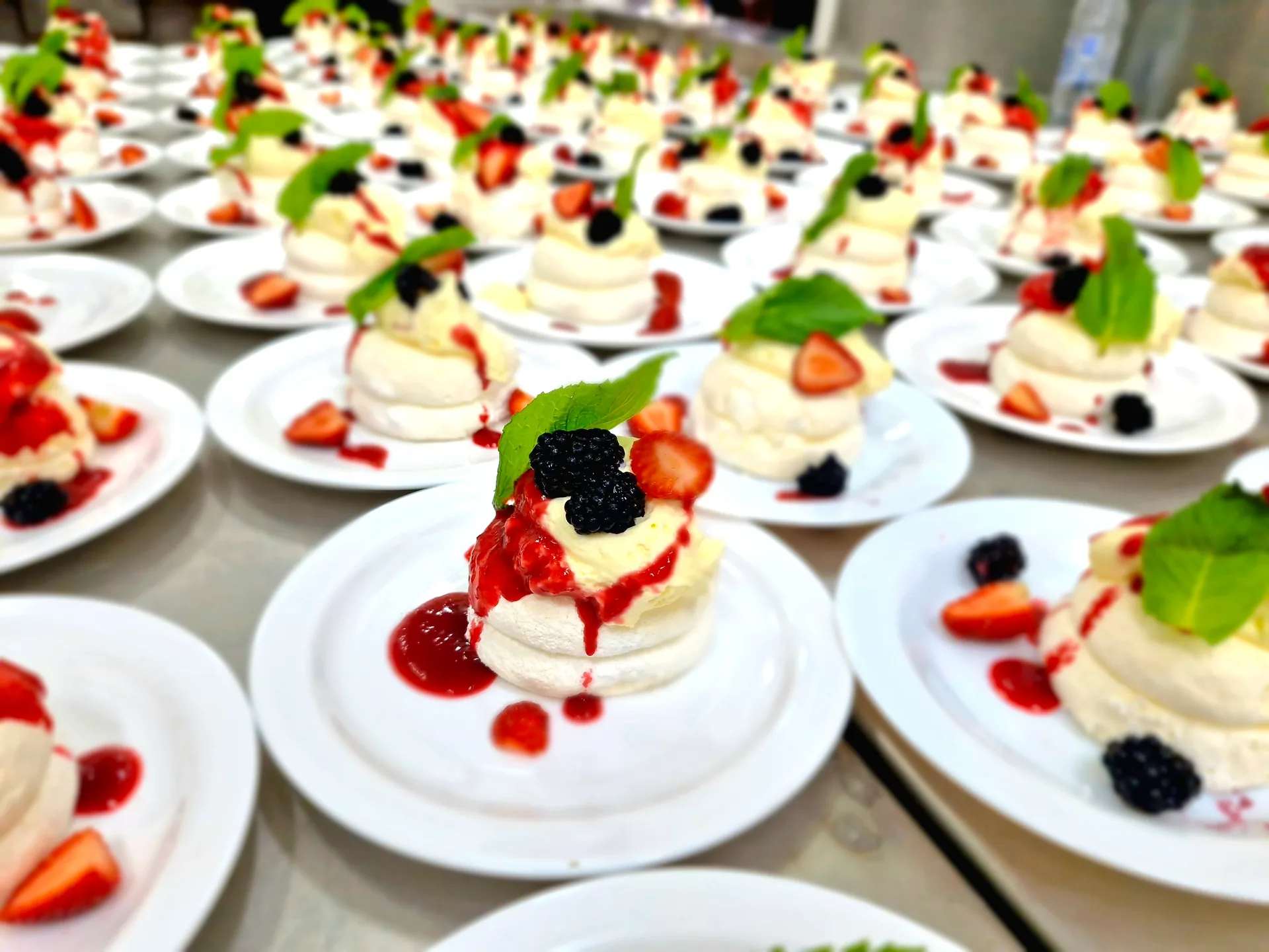 Individual pavlovas with cream and berries being served from a catering menu