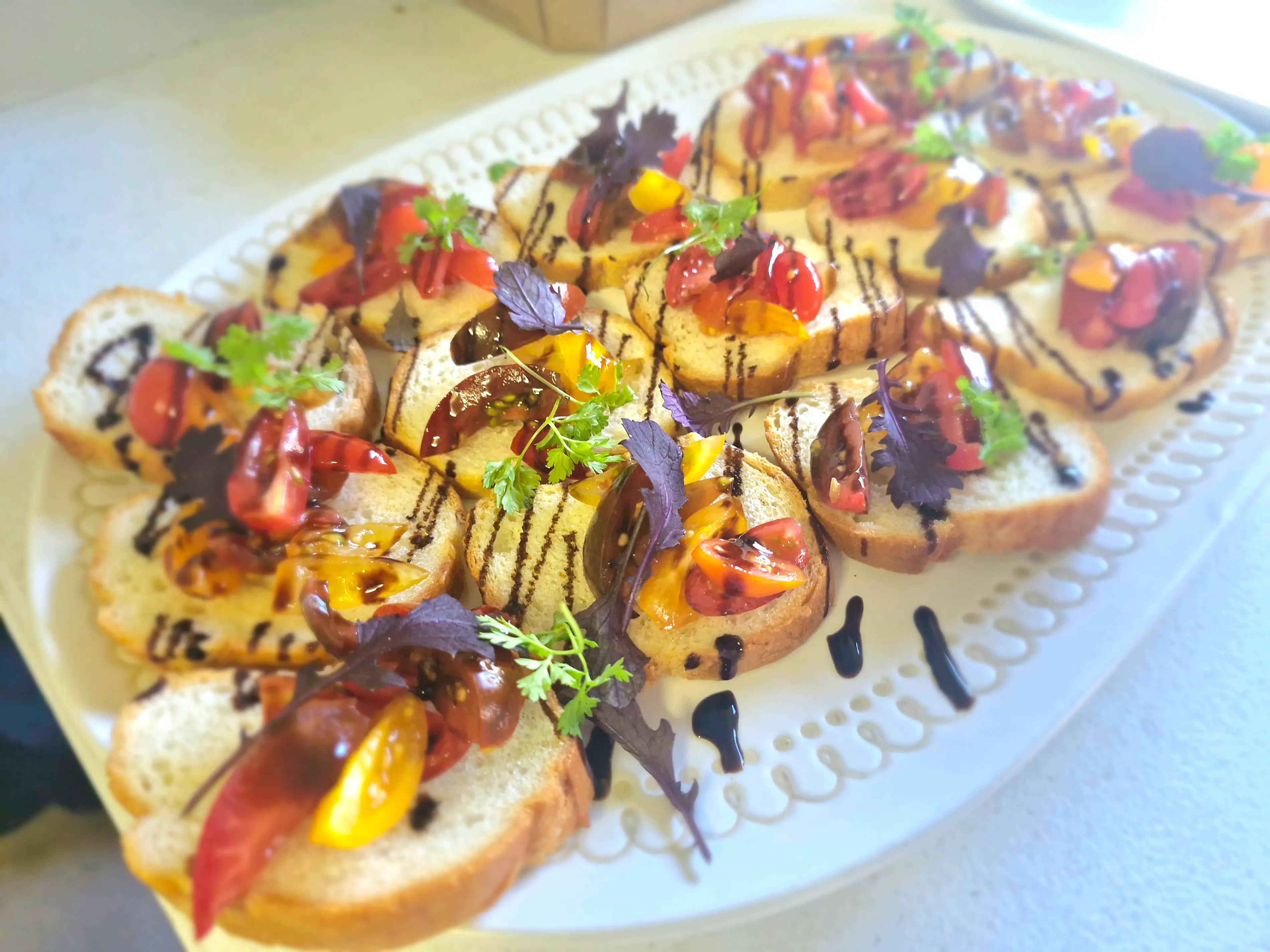 Bruschetta canapés with cherry tomatoes, balsamic glaze and herbs arranged on a white serving platter