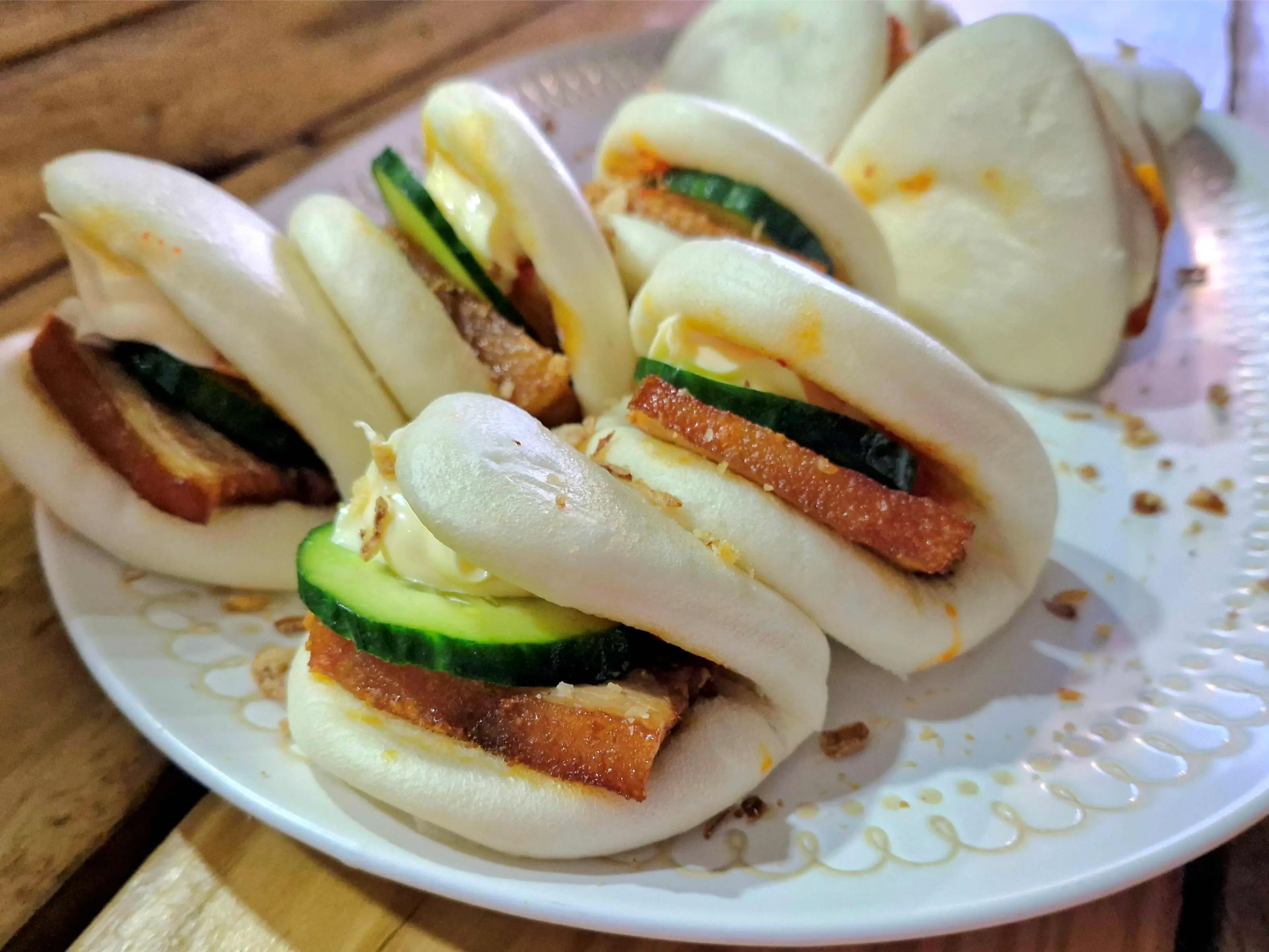 Steamed bao buns filled with pork belly and cucumber on a serving platter